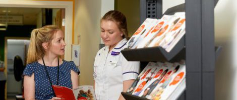 Nurse talking to Librarian whilst looking down at a book. This image is a link to second page of cancer resources.