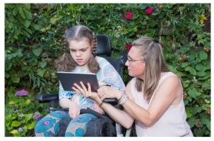 Girl and woman work on  a  computer tablet together. They are in a garden.